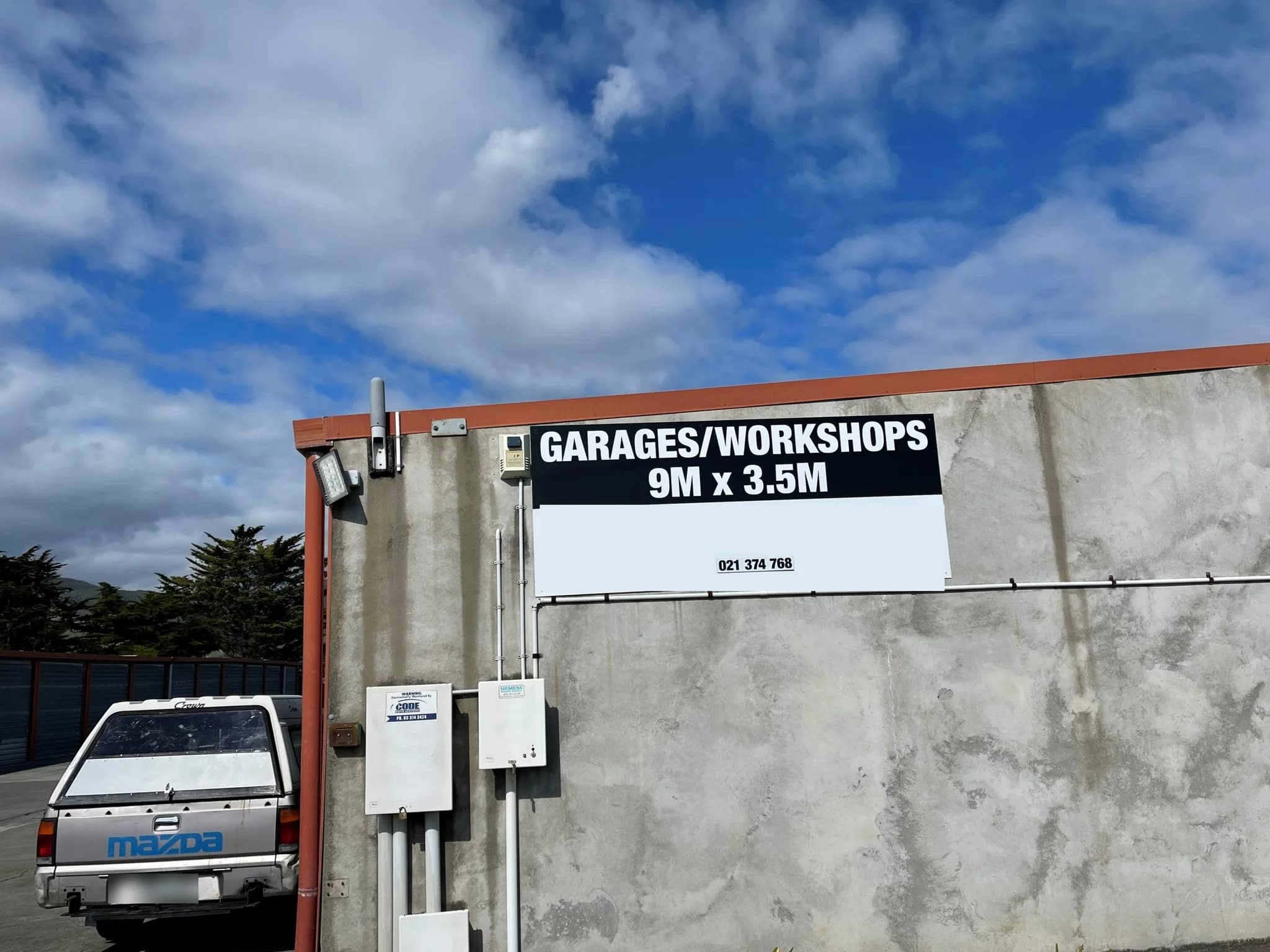 A ute parked beside the tilt-slab concrete units, with a security light and a Garages and Workshops sign